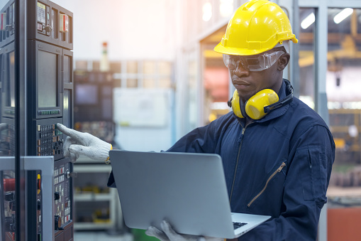 Black engineers wear helmet hat, and carry laptops, inspect and control Systems in the factory.