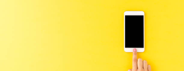 istock Overhead shot of female hand using smartphone with empty screen on yellow background. Banner 1305950156