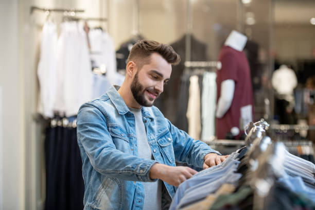 Man shopping in the store Young bearded man choosing new clothes on the rack in shopping mall clothing store stock pictures, royalty-free photos & images