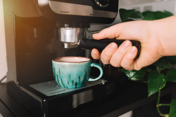 Hand holding portafilter, coffee cup, coffee maker machine, coffee time Hand holding portafilter, green cup of coffee at the coffee maker machine, coffee time. Blurred background. High quality photo espresso maker stock pictures, royalty-free photos & images