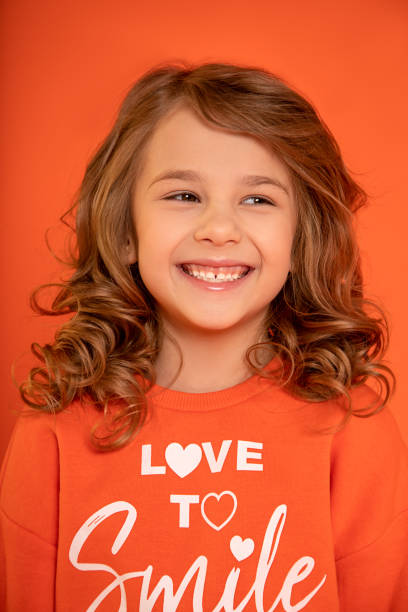 zbliżenie zdjęcie dziewczyny 6-7 lat, doprowadziły do śmiechu na pomarańczowym tle. toothy smile. patrząc w przyszłość. - 6 7 years zdjęcia i obrazy z banku zdjęć