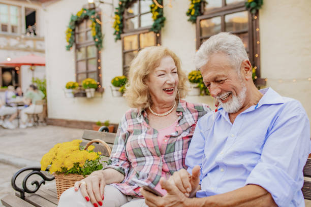 istock Happy senior couple is using mobile phone on the bench and smiling 1305955071