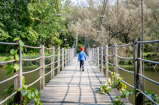 Little Boy Crossing Wooden Suspension Bridge over Lake at Parc national de Plaisance, Quebec, Canada.