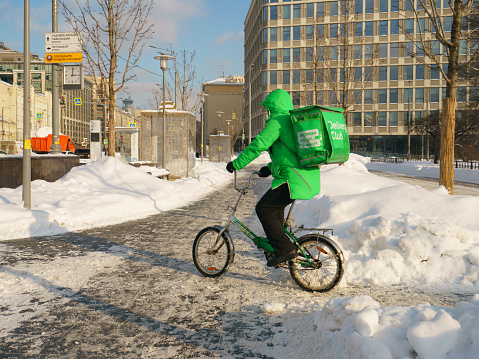 Moscow, Russia - February 18, 2021: Moscow cityscape after blizzard. Huge snowdrifts are everywhere. Typical Russian winter weather. Delivery man cycling. He is working. Lifestyle concept