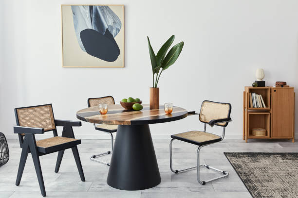 istock Stylish composition of dining room interior with design table, modern chairs, decoration, tropical leaf in vase, fruits, bookcase, abstract mock up paintings and elegant accessories in home decor. 1305956769