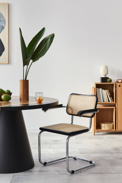 istock Stylish composition of dining room interior with design table, modern chairs, decoration, tropical leaf in vase, fruits, bookcase, abstract mock up paintings and elegant accessories in home decor. 1305956793
