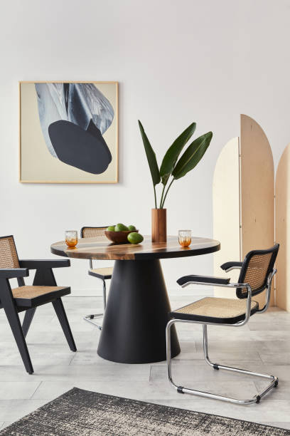 istock Stylish composition of dining room interior with design table, modern chairs, decoration, tropical leaf in vase, fruits, carpet, abstract mock up paintings and elegant accessories in home decor. 1305956882