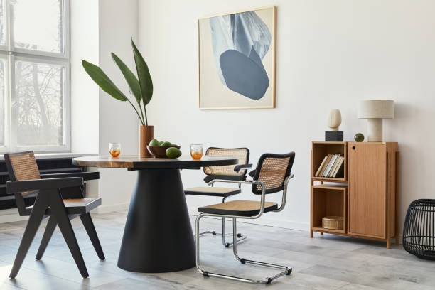 istock Stylish composition of dining room interior with design table, modern chairs, decoration, tropical leaf in vase, fruits, bookcase, abstract mock up paintings and elegant accessories in home decor. 1305956888
