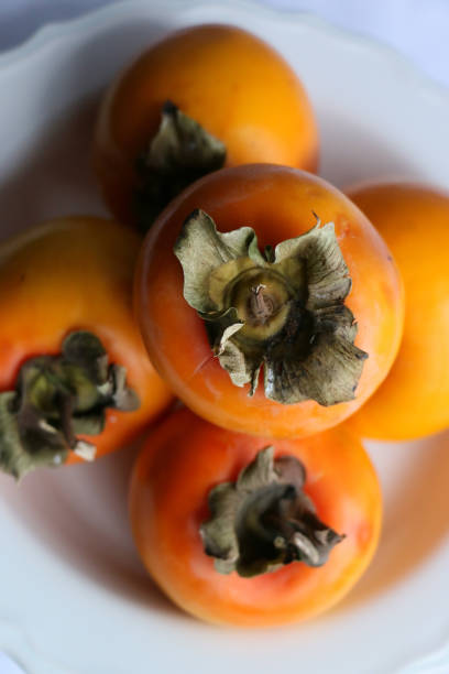 istock Fresh Ripe Persimmons on a White Classic Design Plate, Paradise Palms 1305958332