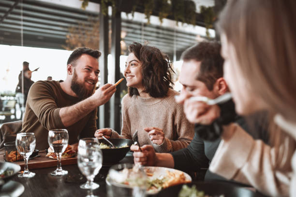 istock Male Feeding His Girlfriend While Having Lunch With Friends In Restaurant 1305959405