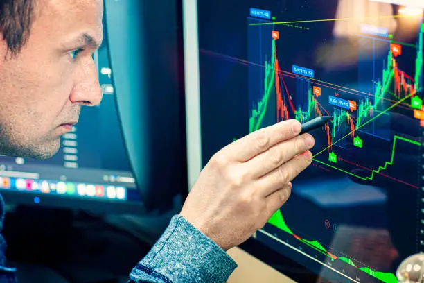 Stockbroker analyzes the financial chart. Online stock exchange on a computer monitor. The economist analyzes the financial graph on the display. A man's hand pointing to an economic chart.