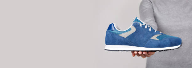 istock Hand with blue sport shoe on grey background. 1305961765