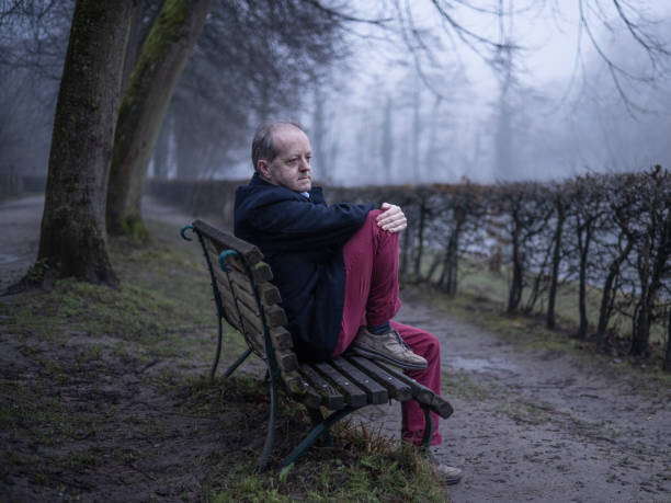 istock With sad face, a middle aged man sits alone on a park bench in a misty forest, lonely and abandoned in gloomy atmospheric mood 1305963532
