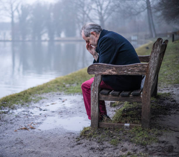 istock Having a headache while sitting on a park bench, a middle aged man alone in misty forest, lonely and abandoned in gloomy atmospheric mood 1305963586