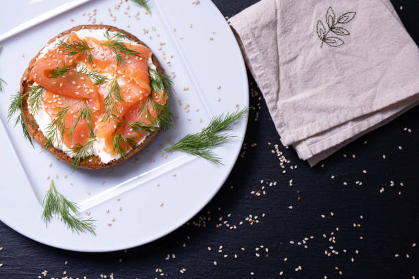 istock plate with bun smeared with fresh cream, smoked fish trout and fresh dill, black background 1305965178