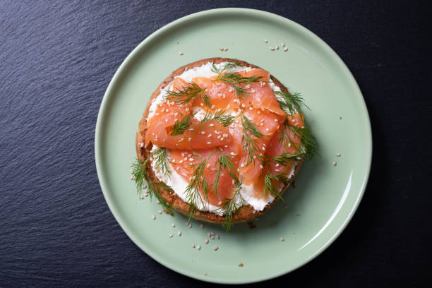 istock half a bun, oiled with fresh cream, garnished with smoked fish and sprinkled with fresh dill and sesame seeds on a green plate and black background 1305965250