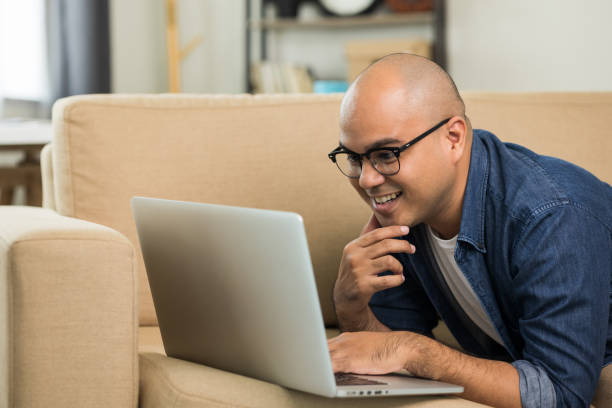 istock Indian man using laptop on sofa in living room texting on laptop sending message or chatting with online social media. 1305967894