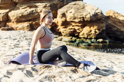 Attractive fitness woman sits on a mat on the beach. Healthy lifestyle