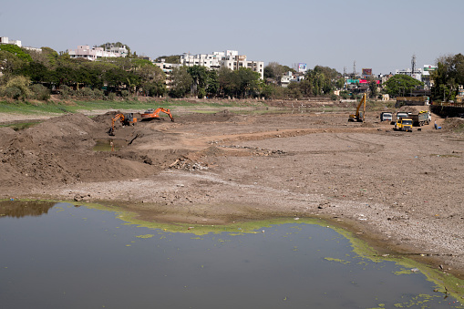 Nashik, Maharashtra, India - March 04 2021: Excavators on a semi-dry bed of the Godavari river dredging the bottom in preparation of the coming monsoon season