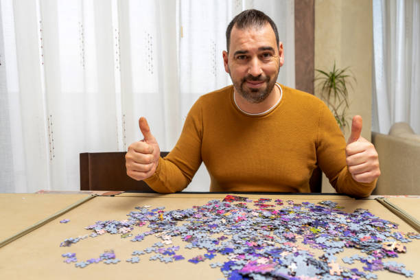 istock Handsome bearded man in an orange sweater with his thumbs up doing a puzzle while smiling looking at the camera 1305971402