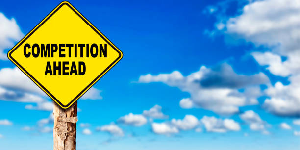 istock Competition ahead road sign with trunk tree, sky background 1305971631
