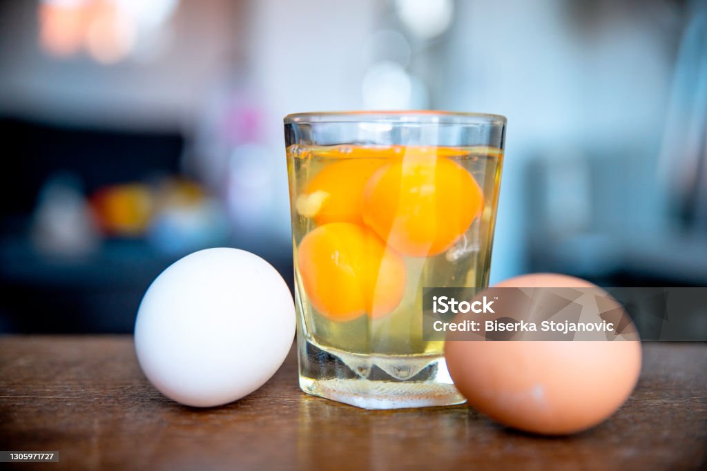 Eggs protein diet Row Eggs in the glass by the white and yellow uncooked egg in the kitchen brown table. close up Animal Egg Stock Photo
