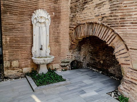 Antique sculpted marble drinking fountain in the wall on Soguk Cesme Sk street in Istanbul, Turkey. Decorative white stone bowl with water and a faucet on the facade of an old Turkish building