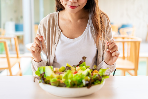 Young woman eating a healthy salad mixes with vegetable and fruit at the restaurant, Healthy lifestyle and diet concept