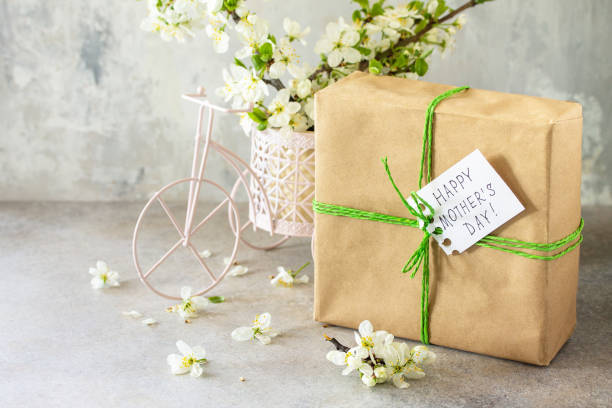 istock Mother's day or womens day background. Blooming cherry branch and a present with a congratulatory inscription that Happy Mother's Day on a gray stone table. Copy space. 1305975621