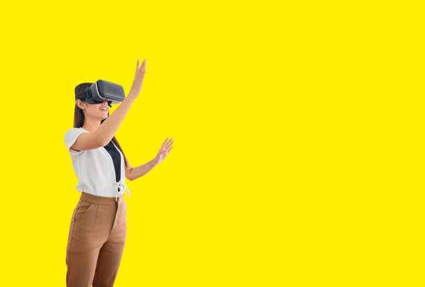 istock Asian woman using VR headset isolated on yellow background with clipping path. Wearing virtual reality headset for playing online game. 1305976449