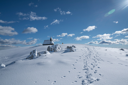 Chapel of Mary of the Snow on Big Pasture Plateau in Slovenia, Europe, with lot of snow and mountains with cloudy blue sky in background.