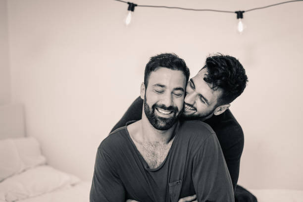 pareja de jóvenes gays que tienen un tierno momento por la mañana en el dormitorio mientras usan pijama - gay man homosexual men kissing fotografías e imágenes de stock