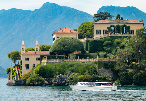 Tourists on a boat admire the Villa del Balbianello in Lenno on Lake Como, Italy. This was a Franciscan monastery around the 12th century but was converted in 1787 to a villa. It has been used in the movies Casino Royale (2006) and Star Wars (2002) among many others. People can be seen on the stairs