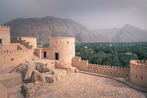 Nakhal,Oman - 04.01.2018: Storm coming to medieval arabian fort of Nakhal, Oman, Arabia. Walls, palm trees and mountains in a haze.