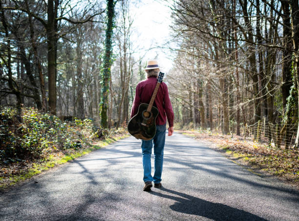 istock Man walking on country road with guitar on his back 1305989648