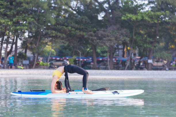 asiatische frau übt yoga auf dem paddelbrett am morgen - activity asia atmosphere beach stock-fotos und bilder