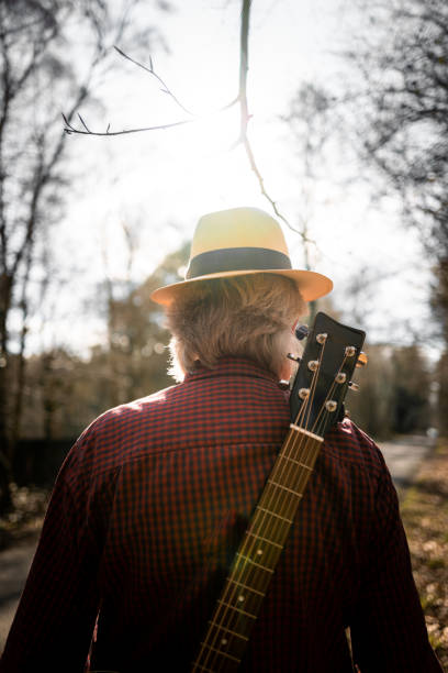 istock Man walking on country road with guitar on his back 1305989653