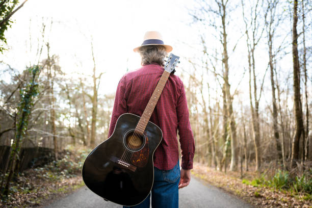 istock Man walking on country road with guitar on his back 1305989662