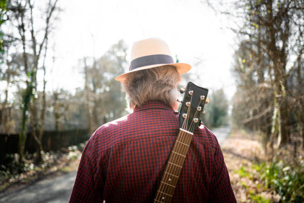 istock Man walking on country road with guitar on his back 1305989664