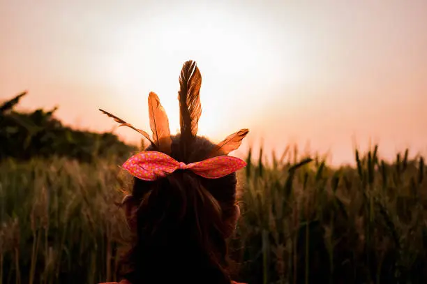 Photo of The Little girl is wearing wild greater coucal bird feathers on her hair on the wheatland beside the countryside river Jalangi in the afternoon.