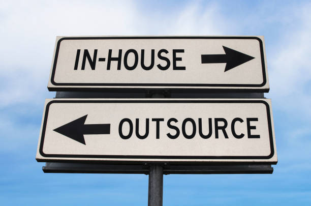 Outsource versus in-house road sign with two arrows on blue sky background. White two streets sign with arrows on metal pole. Directional sign. stock photo