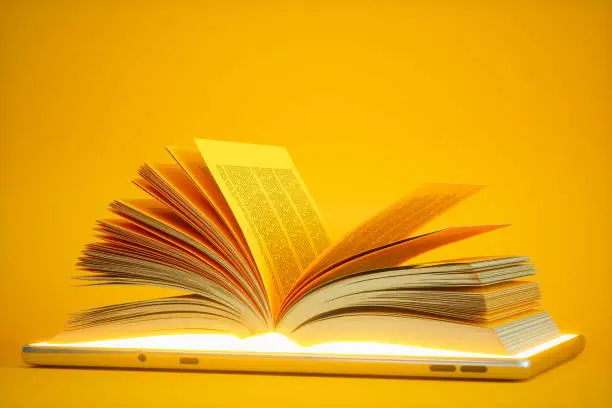 Photo of Audiobook Or E-learning Concept. Open Book On Digital Tablet With Yellow Background.