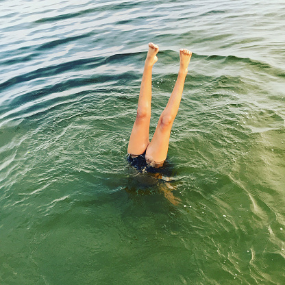 Girl playing in the sea. She stands upside down in the water.