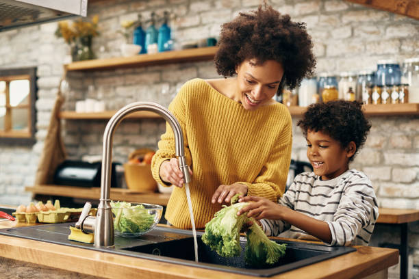 istock Happy black mother and son cleaning vegetables under kitchen sink. 1306001133