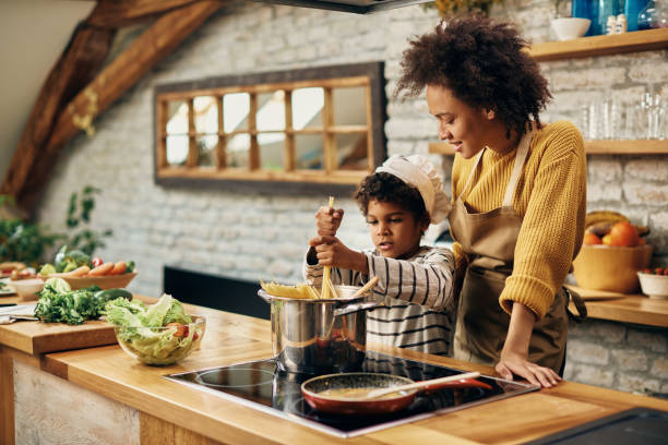 istock Small black boy cooking spaghetti with his mother in the kitchen. 1306001225
