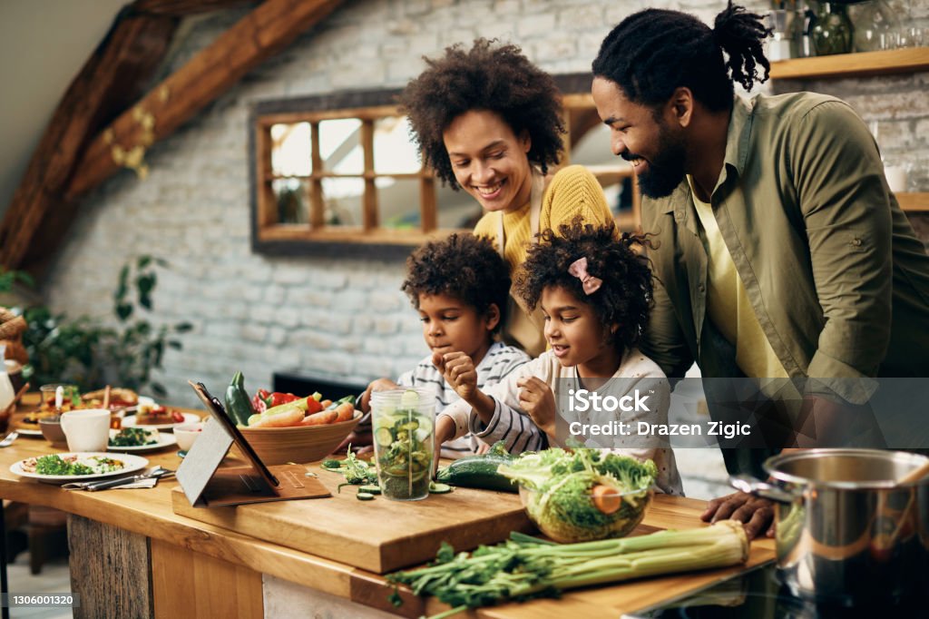 Happy African American family preparing healthy food in the kitchen. Happy black parents and their small kids preparing healthy meal in the kitchen. Family Stock Photo