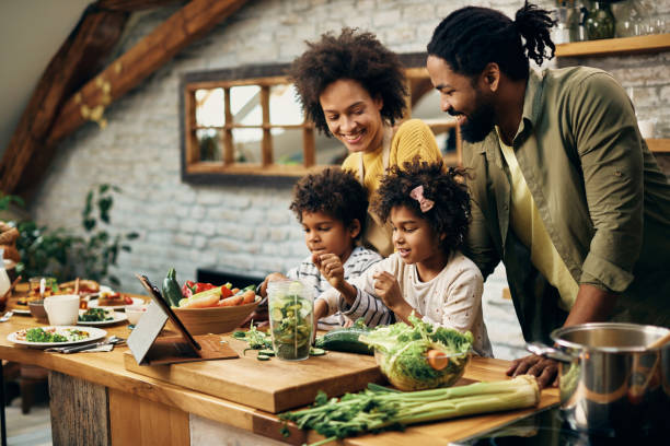 Happy African American family preparing healthy food in the kitchen. Happy black parents and their small kids preparing healthy meal in the kitchen. cooking stock pictures, royalty-free photos & images