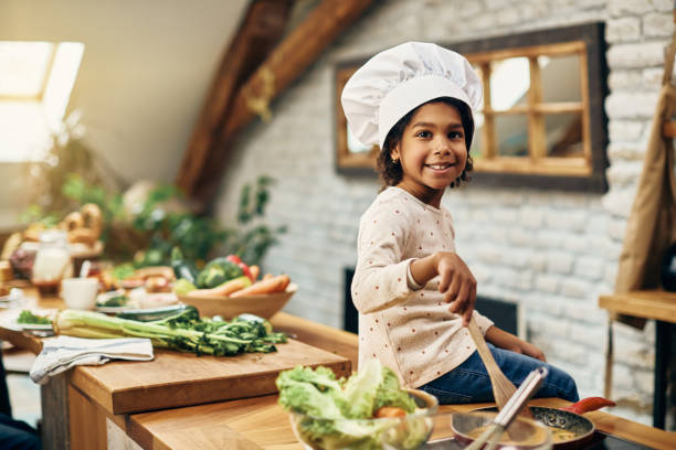 istock Cute black girl wearing chef's hat while preparing scrambled eggs in the kitchen. 1306001351