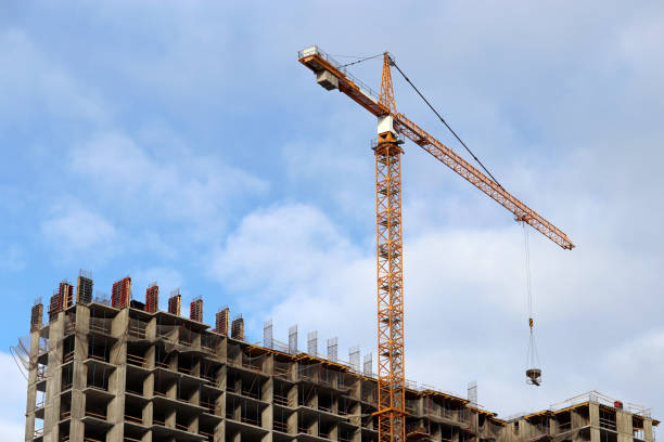 istock Construction crane lifting the cargo above unfinished residential building on blue sky and white clouds background 1306002281