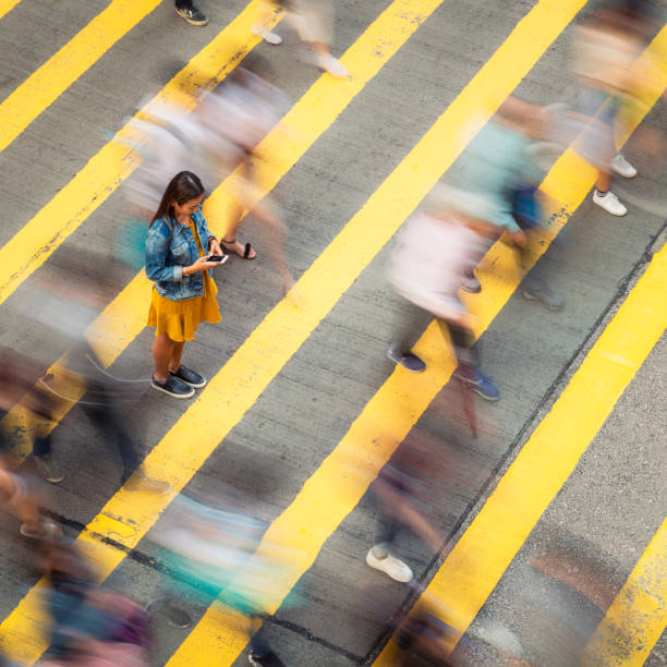 Asking for help A woman, stationary on a crosswalk as people move past her, looking down to her smartphone. mental process stock pictures, royalty-free photos & images